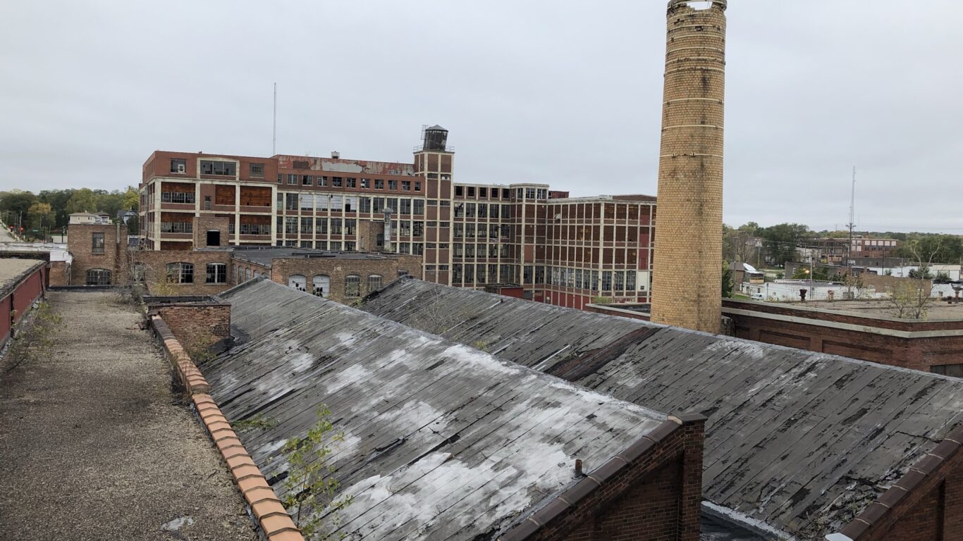 Image shows the Colman Yards campus with an overcast sky in the background and a sawtooth roof structure in the background.